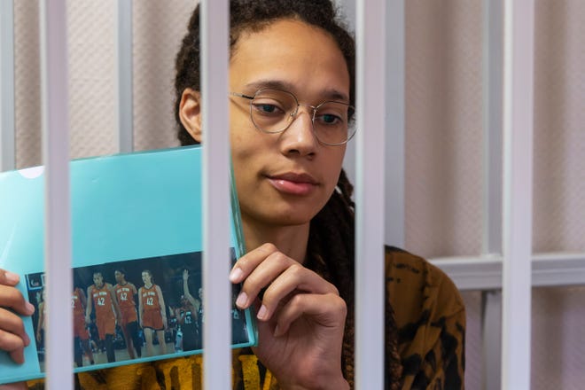 Brittney Griner holds up a photo of players from the recent WNBA All-Star Game wearing her number while sitting in a cage in a Russian court room prior to a hearing on Friday.