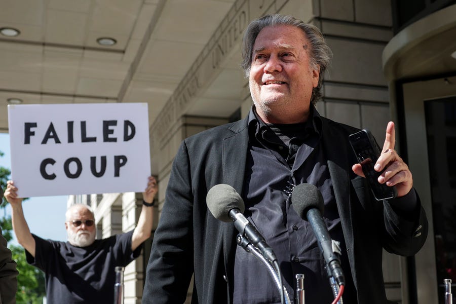 Steve Bannon, advisor to former President Donald Trump, speaks to the media as a protester stands behind him, outside of the E. Barrett Prettyman U.S. Courthouse on June 15 in Washington.