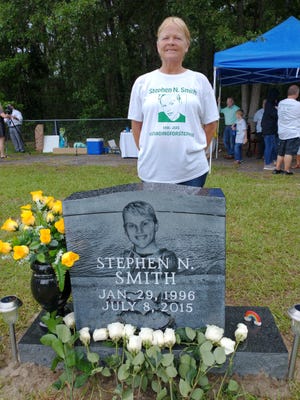 सैंडी स्मिथ अपने बेटे स्टीफन स्मिथ के नए स्मारक के पीछे मुस्कुरा रही हैं।