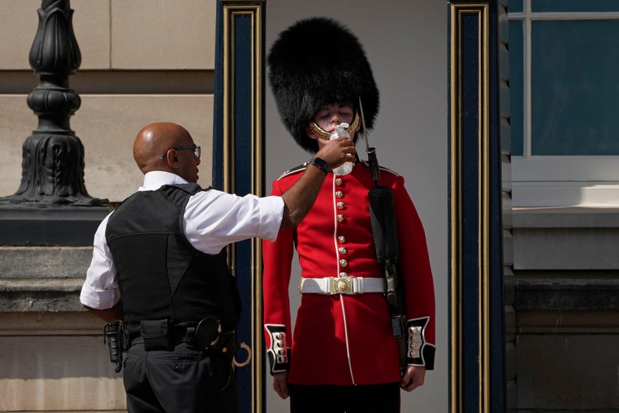 A police officer gives water to a British soldier wearing a traditional bearskin hat, on guard duty outside Buckingham Palace, during hot weather in London. The British government has issued its first-ever "red" warning for extreme heat.