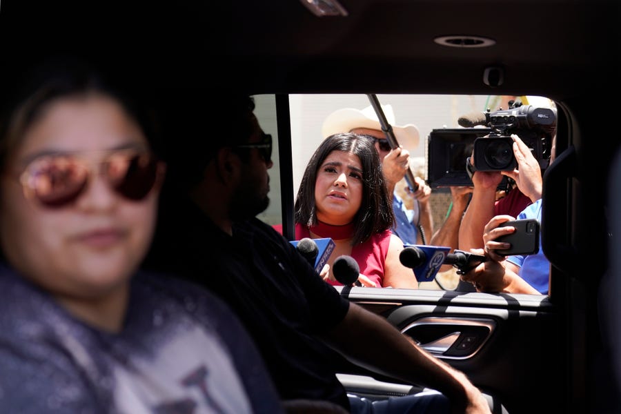 Crystal Garcia, left, and Sergio Garcia, center, stepmother and father of shooting victim Uziyah Garcia, talk to the media from the back of a vehicle after picking up a copy of the Texas House investigative committee report on the shootings at Robb Elementary School, Sunday, July 17, 2022, in Uvalde, Texas.