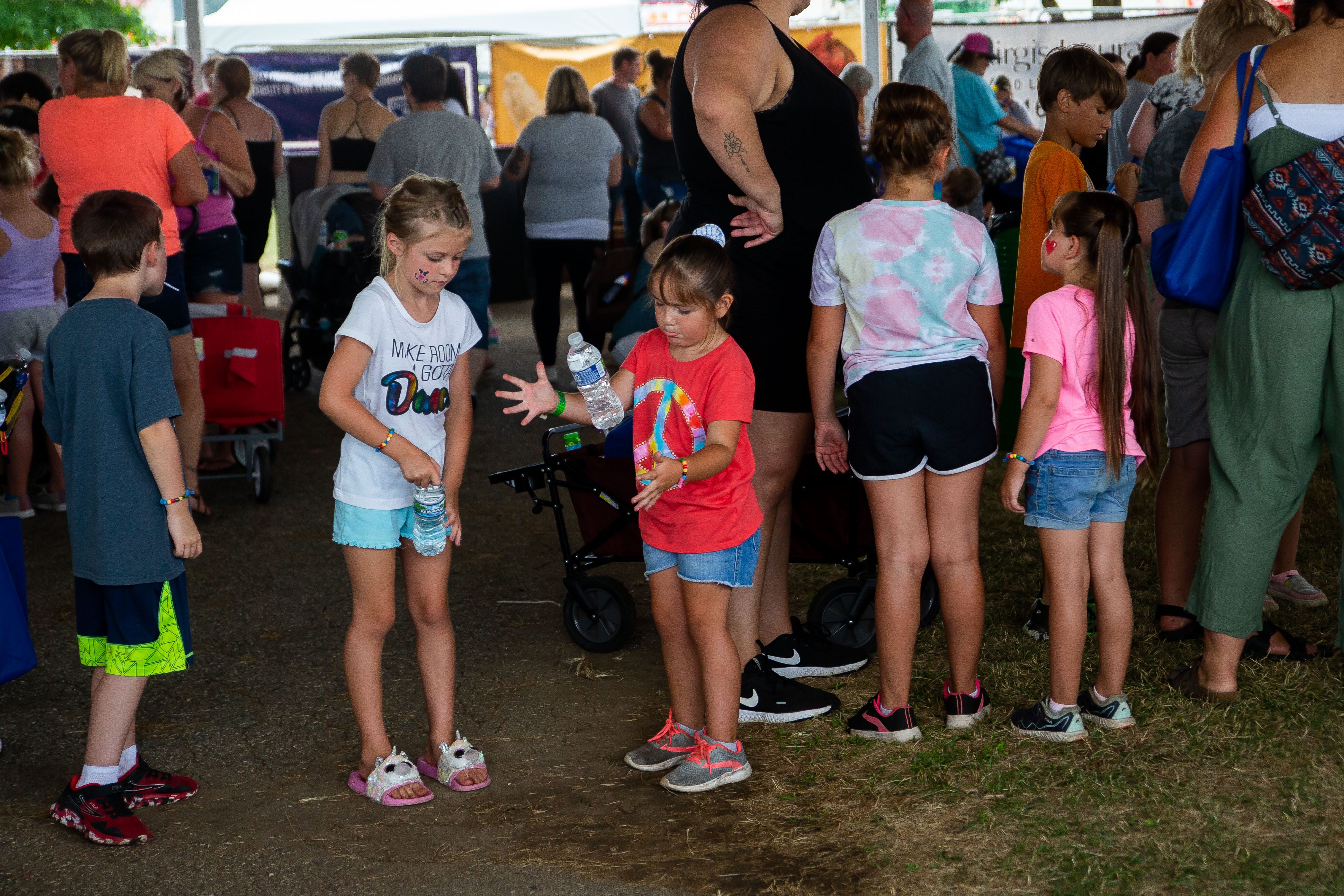 Children flip their water bottles while they wait in line for a balloon animal Tuesday, July 19, 2022, at the Ionia Free Fair. Hundreds of families gather for games, activities and more during Kids Day at the Free Fair.