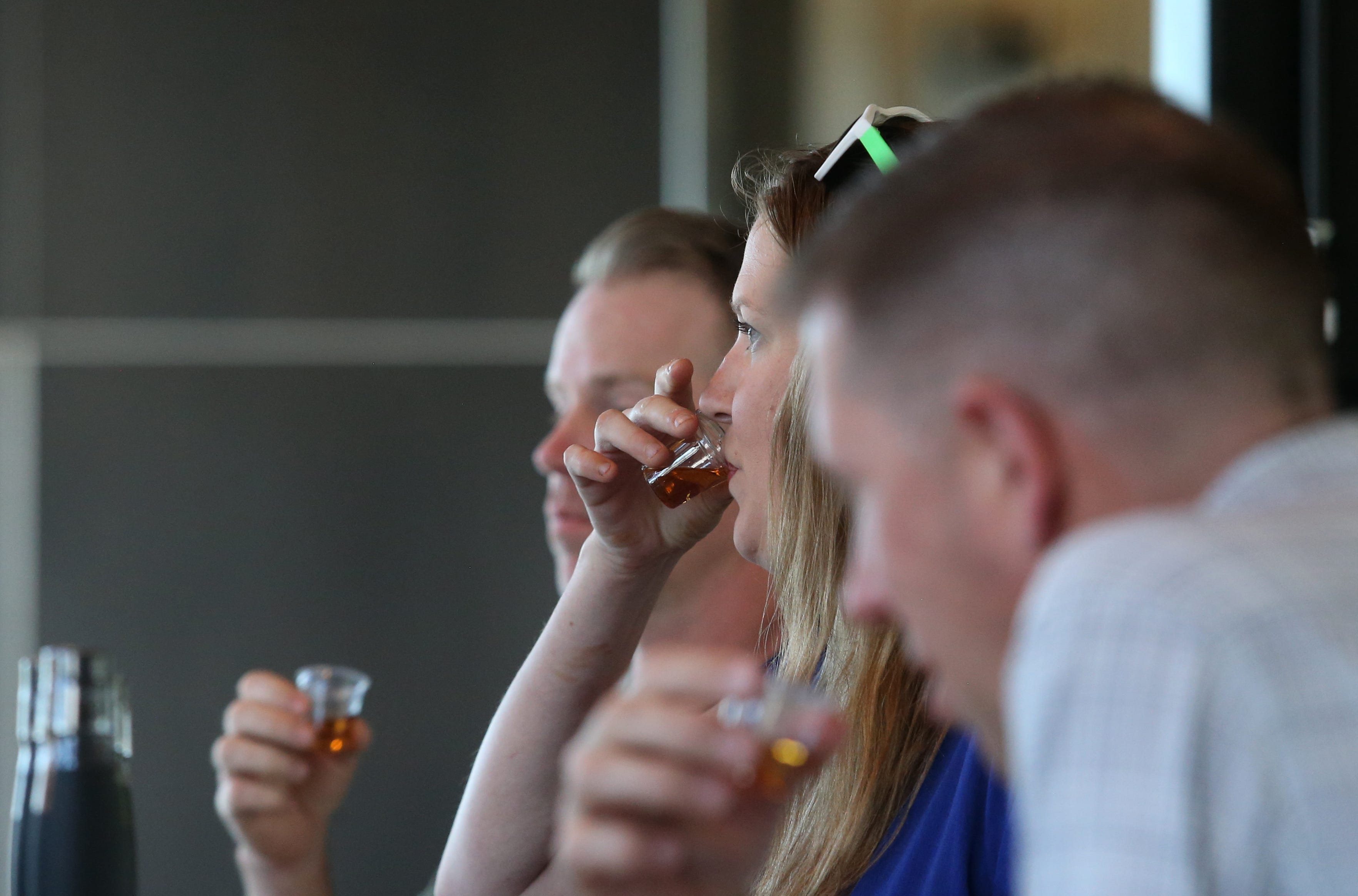 Maggie Menderski, center, Chris L’Heureux, right, and Mike Day take drinks of bourbon at the end of the tour of New Riff Distillery in Newport, Kentucky.June 30, 2022