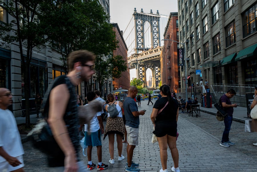 People walk through city streets within view of the Manhattan Bridge on a sweltering afternoon as temperatures reach into the 90s on July 20, 2022 in the Brooklyn borough of New York City.