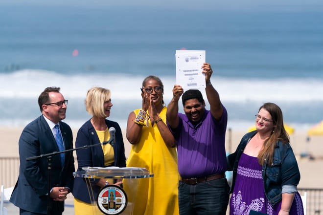 Anthony Bruce, second from right, a great-great grandson of Charles and Willa Bruce, holds up the title deed of the oceanfront property known as Bruce's Beach during a dedication ceremony in Manhattan Beach, Calif., Wednesday, July 20, 2022, as he is joined by wife, Sandra, from right, Los Angeles County officials, Holly J. Mitchell, Janice Hahn and Dean Logan. Los Angeles County officials on Wednesday presented the deed to prime California oceanfront property to heirs of the Black couple who built a beach resort for African Americans but were harassed and finally stripped of the land nearly a century ago.
