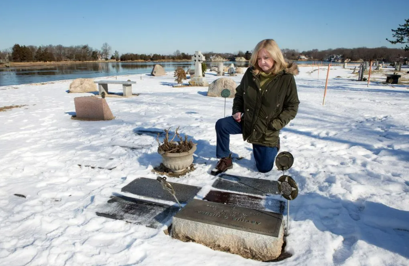 Mary Nisula kneels in front of her family's graves at Cohasset Central Cemetery during the winter of 2020. The graves of her son, parents and sister were all being flooding before a seawall was constructed.