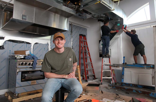 Charlie Denk, the founder and owner of Stir Studio Kitchen, sits inside his new Hudson location as Arman Loktev and Anthony Karasik of Ohio Fire Suppression install a kitchen hood and fire suppression system.