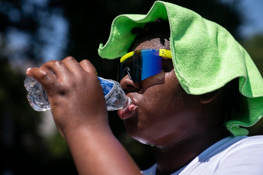 Amir Brown, 15, tries to cool down while helping his mother set up a stand selling cold drinks near the National Mall on Friday, July 22, 2022, in Washington.