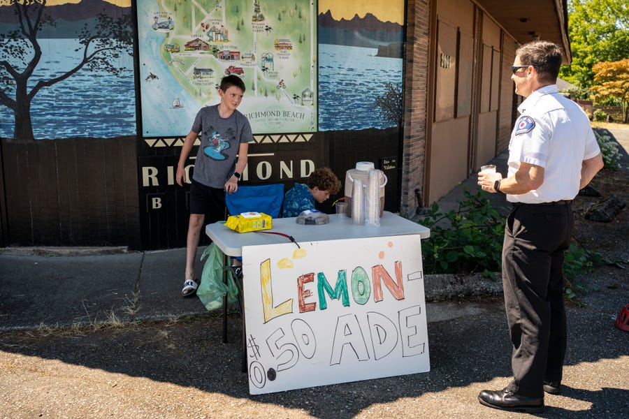 Gabe DeBay, Medical Services Officer with the Shoreline Fire Department, buys lemonade from Kaellan Robberts and Aven Josephy on July 26, 2022, in Shoreline, Washington. The Pacific Northwest is experiencing a heat wave with potentially record-breaking temperatures, which is expected to last for the rest of the week.