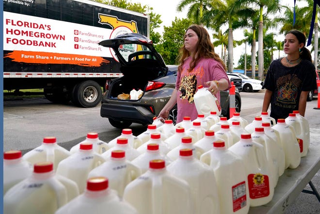 Vanessa Correa, left, and Gigi Fiske, right, pass out gallons of milk at a food distribution held by the Farm Share food bank, Wednesday, July 20, 2022, in Miami. Long lines are back at food banks around the U.S. as working Americans overwhelmed by inflation turn to handouts to help feed their families. (AP Photo/Lynne Sladky)