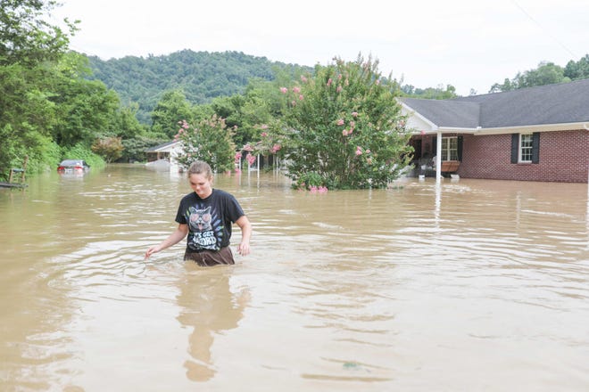 A young woman walks through medium-deep water next to a house that was flooded by water from the North Fork of the Kentucky River in Jackson, Kentucky, on July 28, 2022.  At least eight people have died after torrential rains caused massive flooding in eastern Kentucky, leaving several people stranded on rooftops and in trees, the state governor of the southeastern US said Thursday.