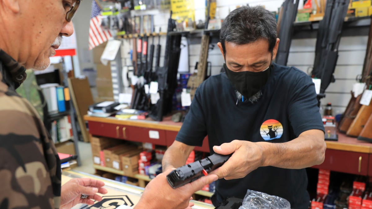 A clerk hands a gun to a customer inside a gun shop, Thursday, June, 23, 2022 in Honolulu. In a major expansion of gun rights after a series of mass shootings, the Supreme Court said Thursday that Americans have a right to carry firearms in public for self-defense. (AP Photo/Marco Garcia)m ORG XMIT: HIMG109