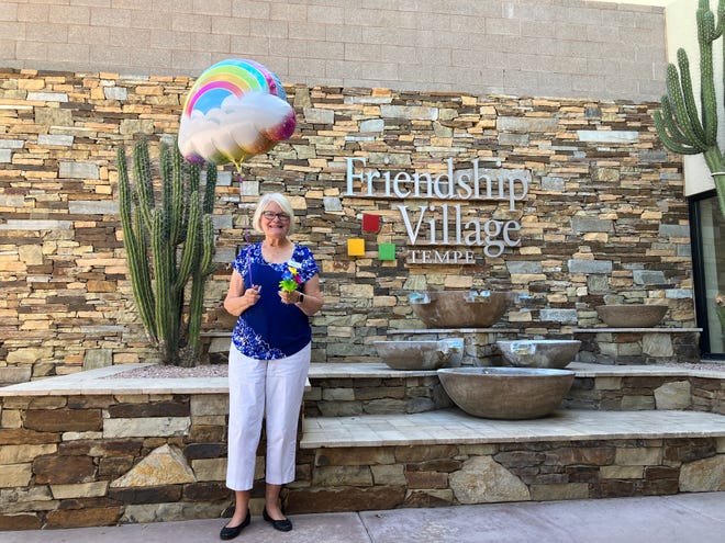 Lida Mainieri with a rainbow balloon and flowers, stands outside at Friendship Village, Tempe.