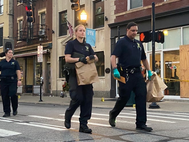 Cincinnati police officers carry evidence bags in Over-the-Rhine on Sunday morning. Police say at least nine people were injured in a shooting outside Mr. Pitiful's bar at 13th and Main streets at about 1:40 am