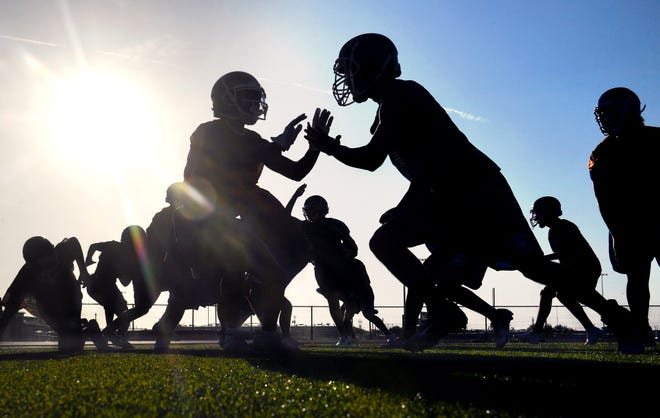 Football players are silhouetted as they practice in the early morning sun at Cooper High School on Monday.