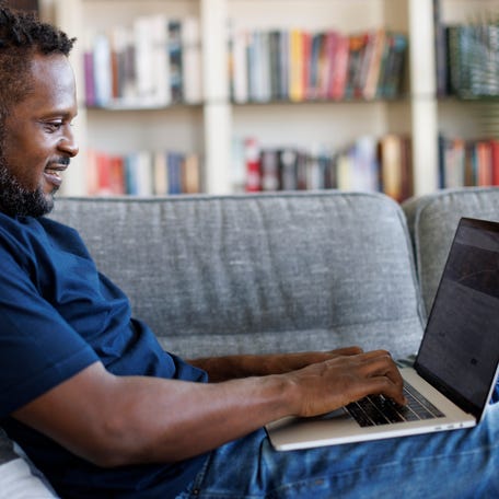 Smiling man sitting on a sofa and using a laptop.