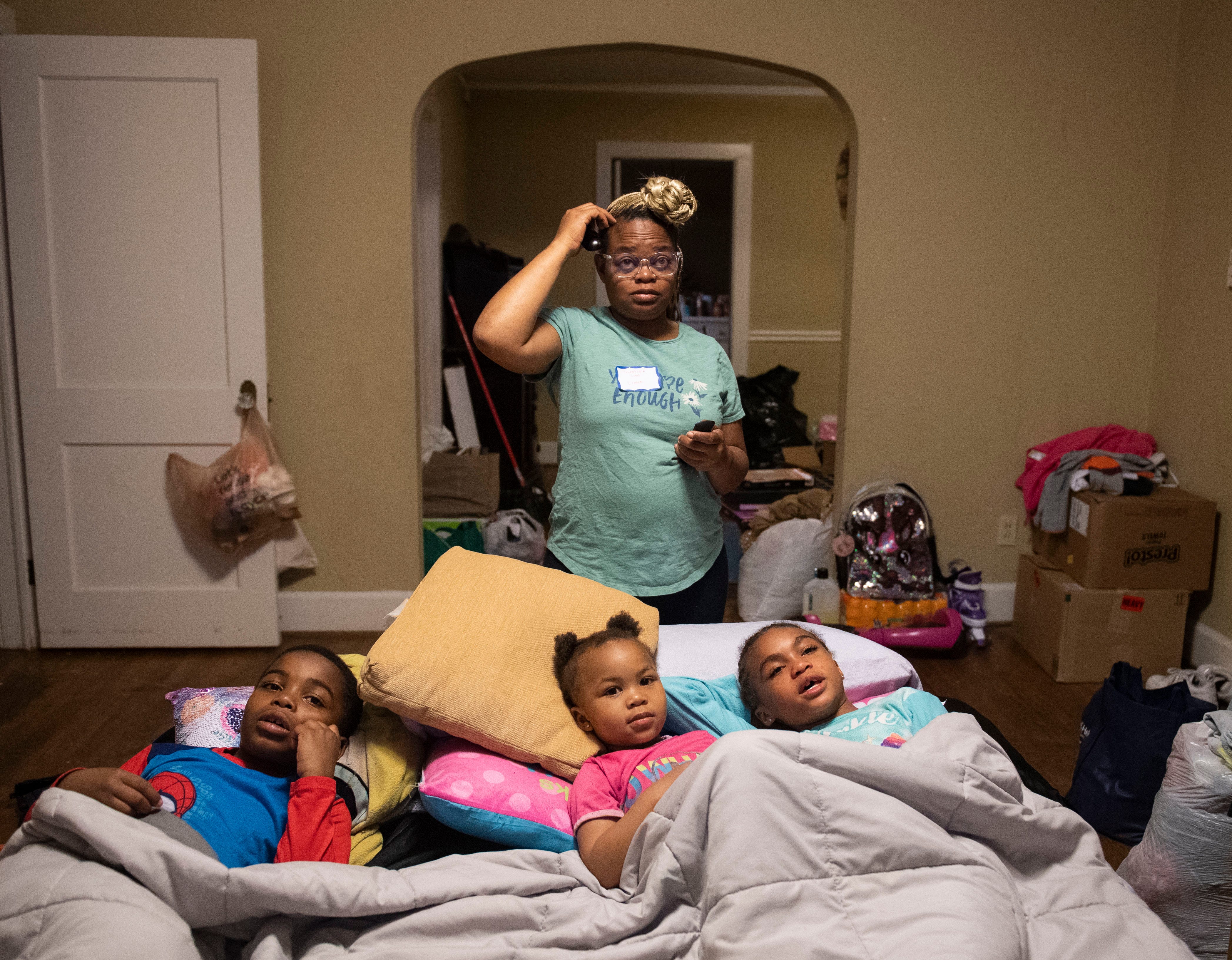 Quentoria stands behind her three children, who are laying together in a bed