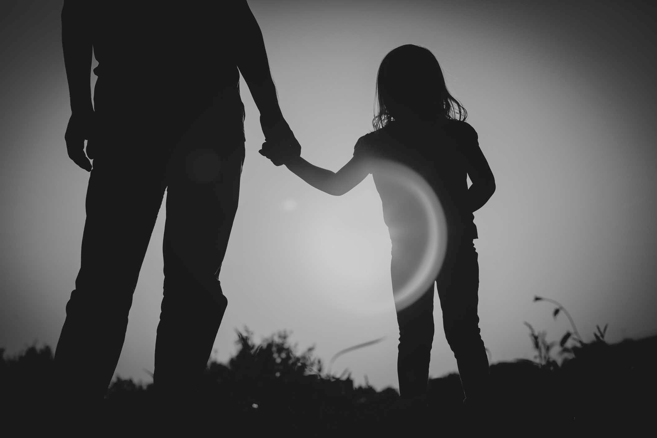 silhouette of little girl holding parent hand at sunset, parenting concept