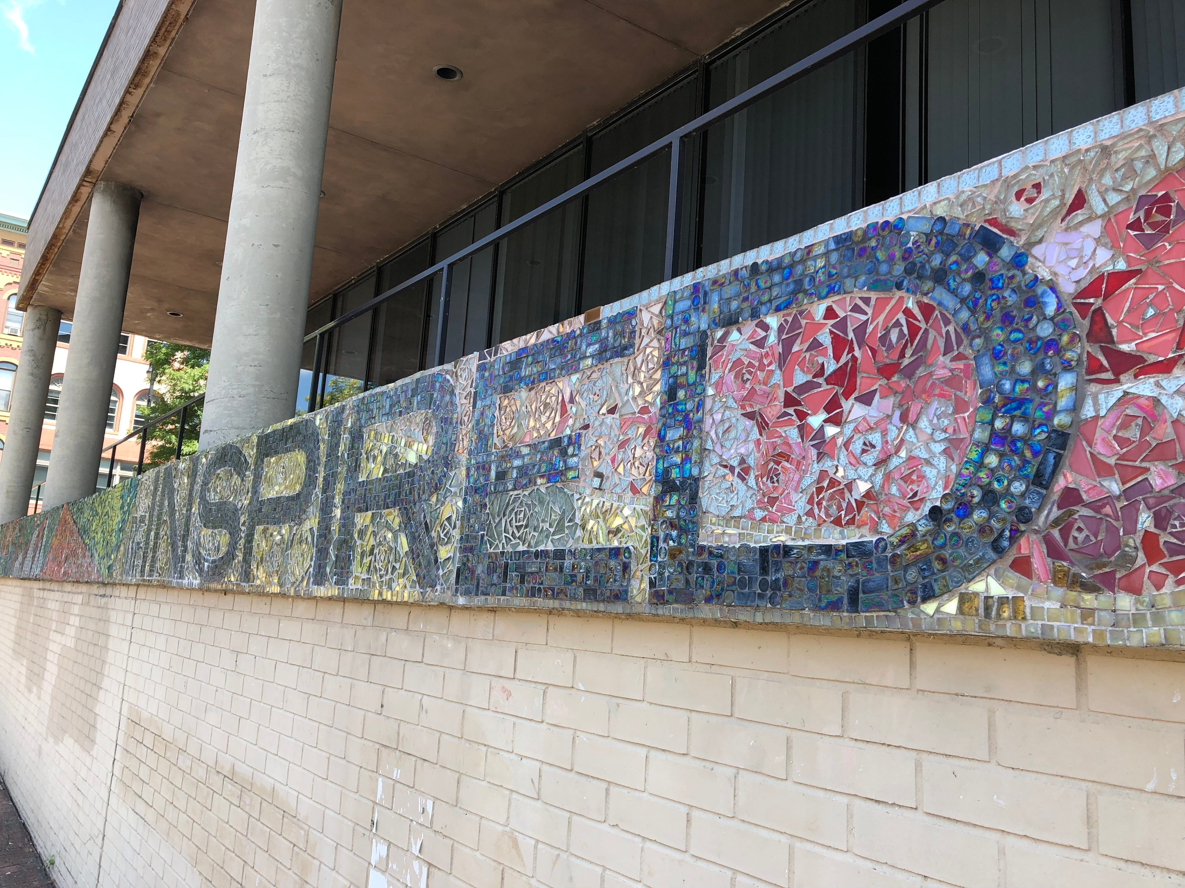 Facing the Chenango River, the edge of 2 Court St. in Binghamton is decorated with small pieces of colored glass. Artist Emily Jablon included the phrase 'Be Inspired, Be Binghamton' in the completed mosaic.