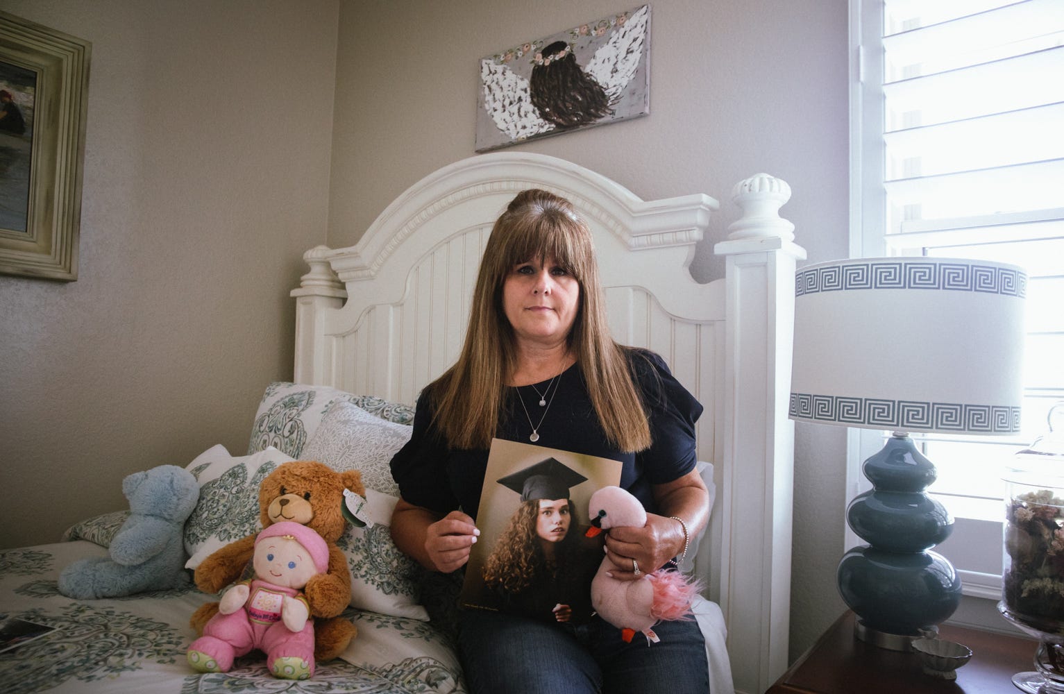 Joann Pierson poses sitting on a bed next to a handful of stuffed animals, holding a photo of her daughter, 36-year-old Kristi Norris, who died at a D&S Residential Services Group home in October 2020.