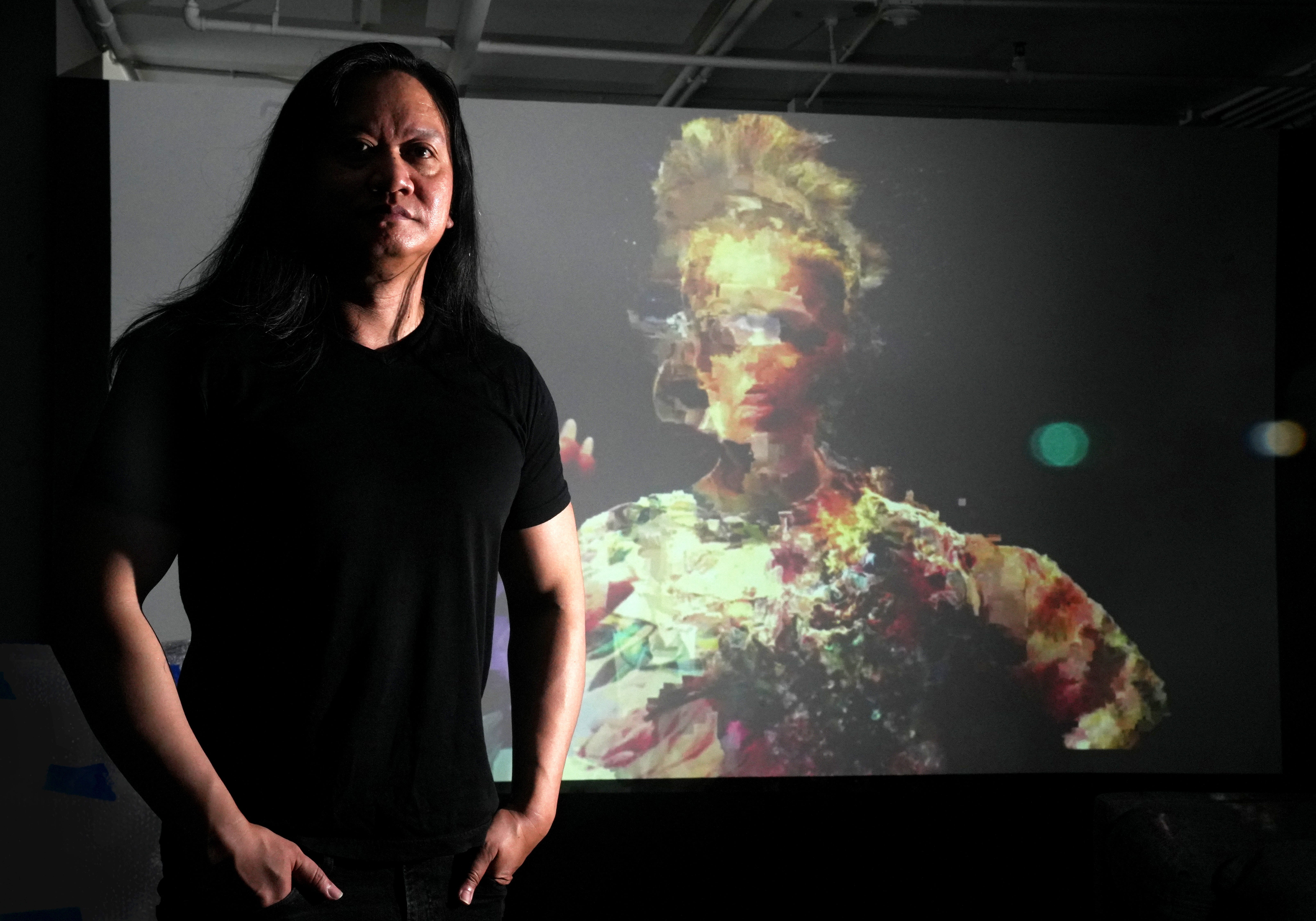 Rembrandt Quiballo, stands next to his piece entitled My Love, projected inside the Fine Art Complex in Tempe on Wednesday, Aug. 24, 2022. Quiballo is a digital artist who was born in the Philippines, traveled the world and eventually settled in Arizona. Quiballo tackles questions of religion, myth, and technology in his digital images.