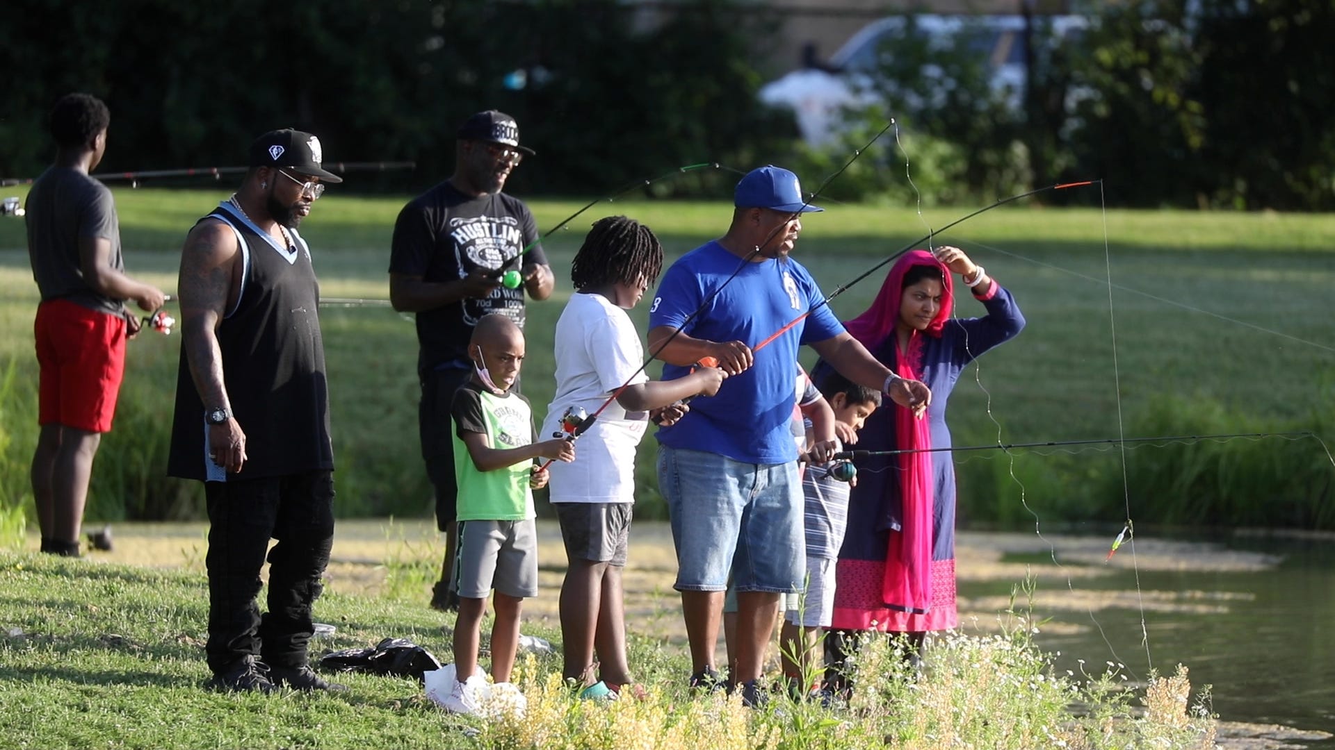 Pastor Kenneth Simmons of Cold Spring Bible Chapel in Buffalo, NY helps a youth at Schiller Park haul in a fish on June 29, 2022.  With the help of some of the MAD DADS and Buffalo Police Athletic League, they took young boys fishing.  They also taught anyone else that was interested like the woman and her son who were at the park.   Simmons has a mentoring program that during the summer young boys will fish, go on outings and grow vegetables in a raised box behind his church.