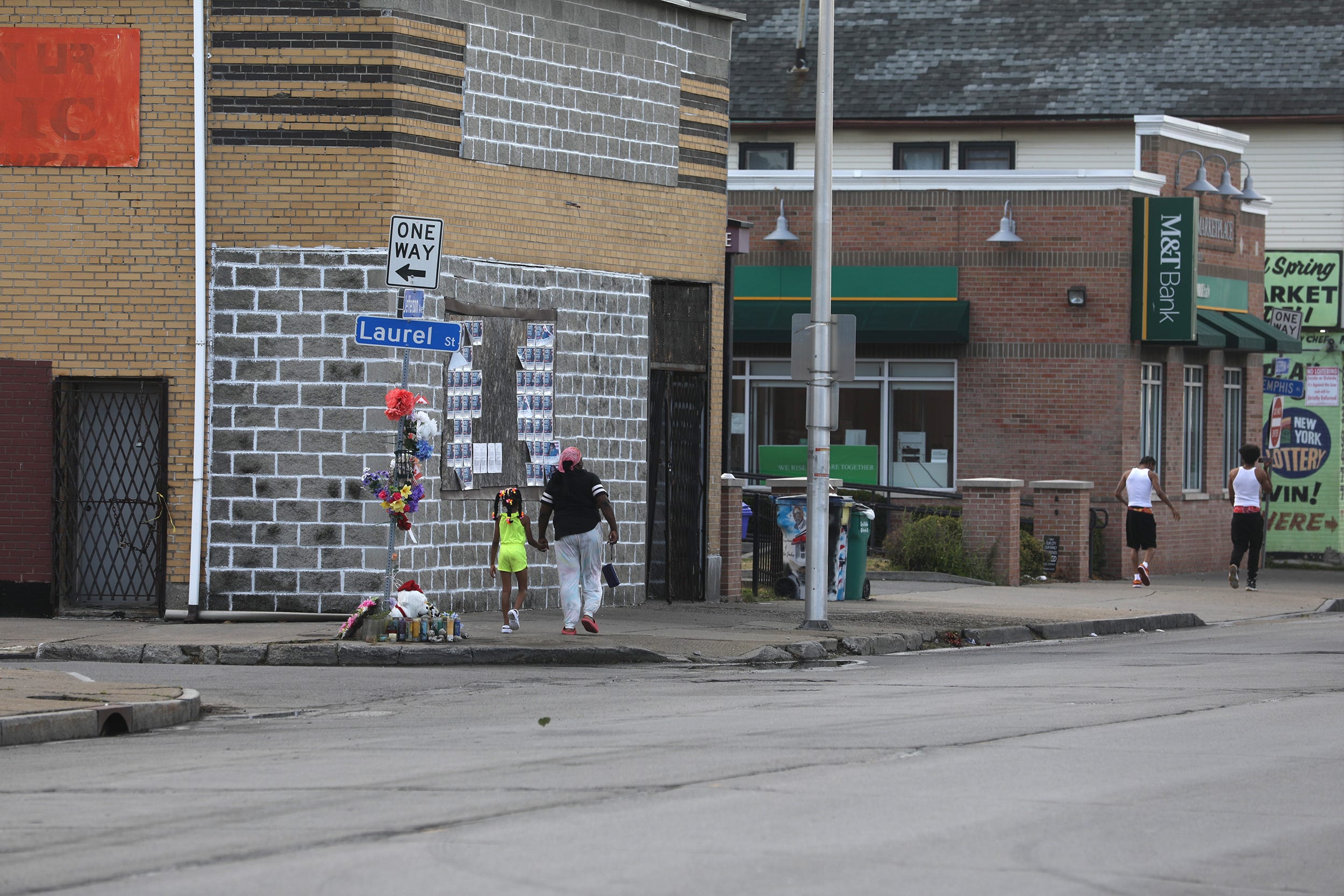 Residents on Tuesday, July 12, 2022, walk by the memorials on Jefferson Avenue in Buffalo, N.Y., on their way home. The memorials were for those who died in a racist attack at Tops Friendly Market, located across the street. A white man came to the predominantly Black neighborhood on May 14 purposely to kill Black people. He targeted the Tops and killed 10 and injured three others.