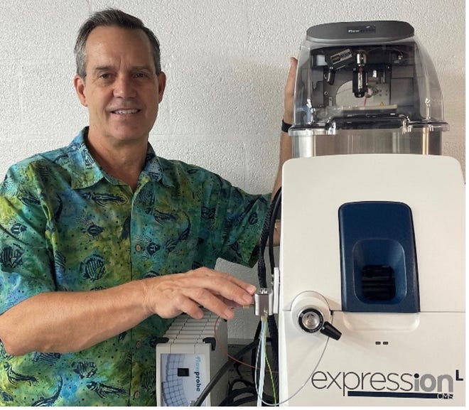 Gary Van Berkel standing next to a Van Berkel Ventures, LLC mass spectrometer fitted with both an Advion Touch Express Open Port Sampling Interface (right hand, front) and a Prosolia flowprobe (left hand, top back). Both commercial products are based on his inventions.