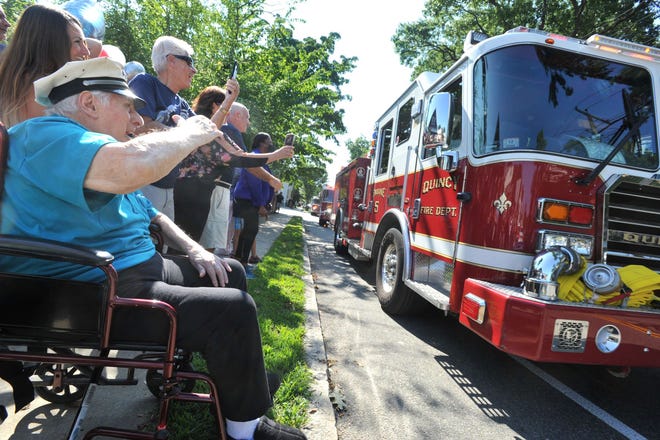 Quincy Fire Chief Lieutenant Lou Mulvesti waves at a parade of fire trucks past Quincy's home in celebration of Quincy's 99th birthday, Friday, August 26, 2022.