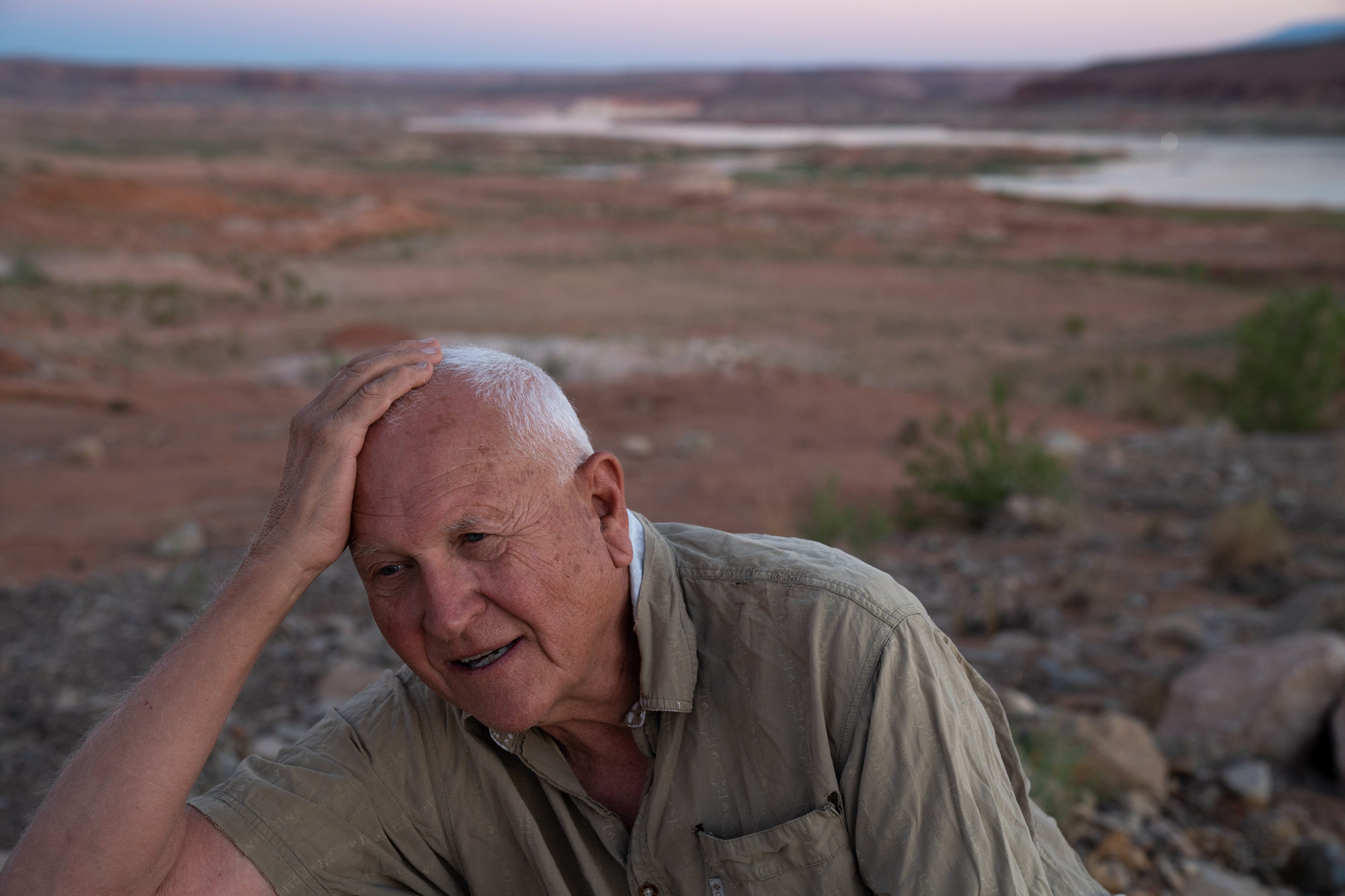 A close up image of Jack Schmidt, wearing a tan button up shirt, with Lake Powell and it's rocky shores in the background.