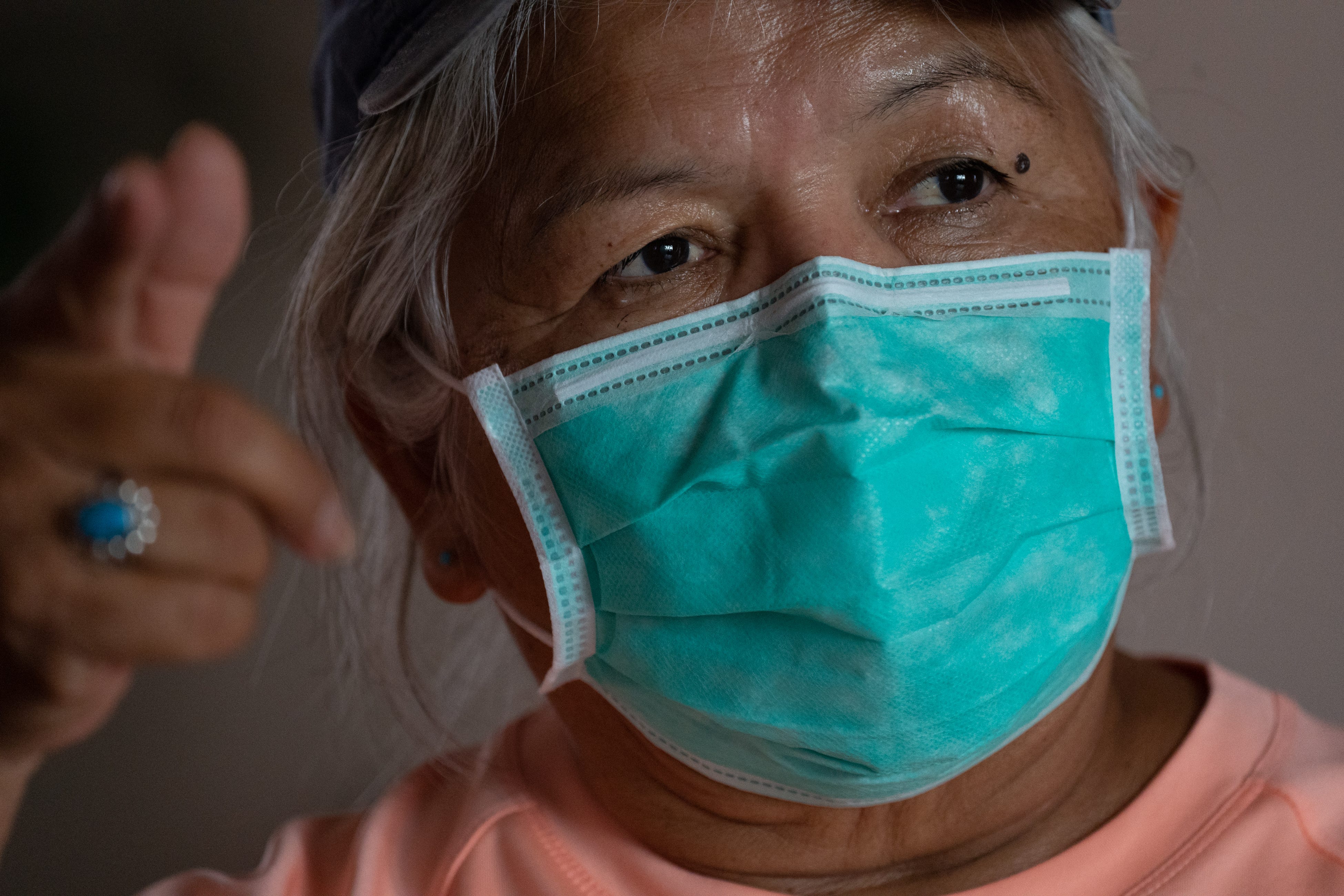 A close up image of JoAnne Yazzie-Pioche, who is wearing a teal mask and peach shirt. She is gesturing while she talks.