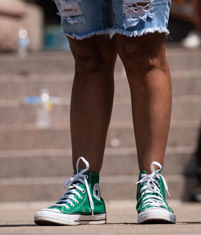 Relatives of Maite Rodriguez, a 10-year-old victim of the May mass shooting in Uvalde, wear green Converse sneakers in tribute to her as they speak on the steps of the Capitol on Aug. 27 to demand that Gov. Greg Abbott call a special legislative session to raise the minimum age to purchase an AR-15-style rifle.