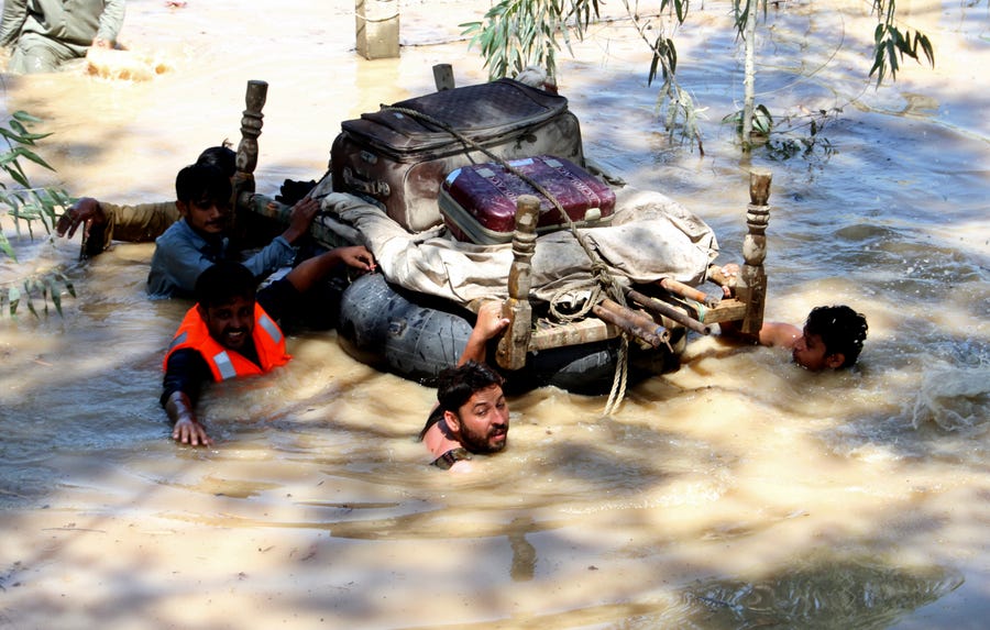 Displaced people float belongings salvaged from flood-hit homes through a flooded area, on the outskirts of Peshawar, Pakistan, Sunday, Aug. 28, 2022. Officials in Pakistan say deaths from widespread flooding have topped 1,000 since mid-June. Flash flooding from the heavy rains has washed away villages and crops as soldiers and rescue workers evacuated stranded residents to the safety of relief camps and provided food to thousands of displaced Pakistanis. 