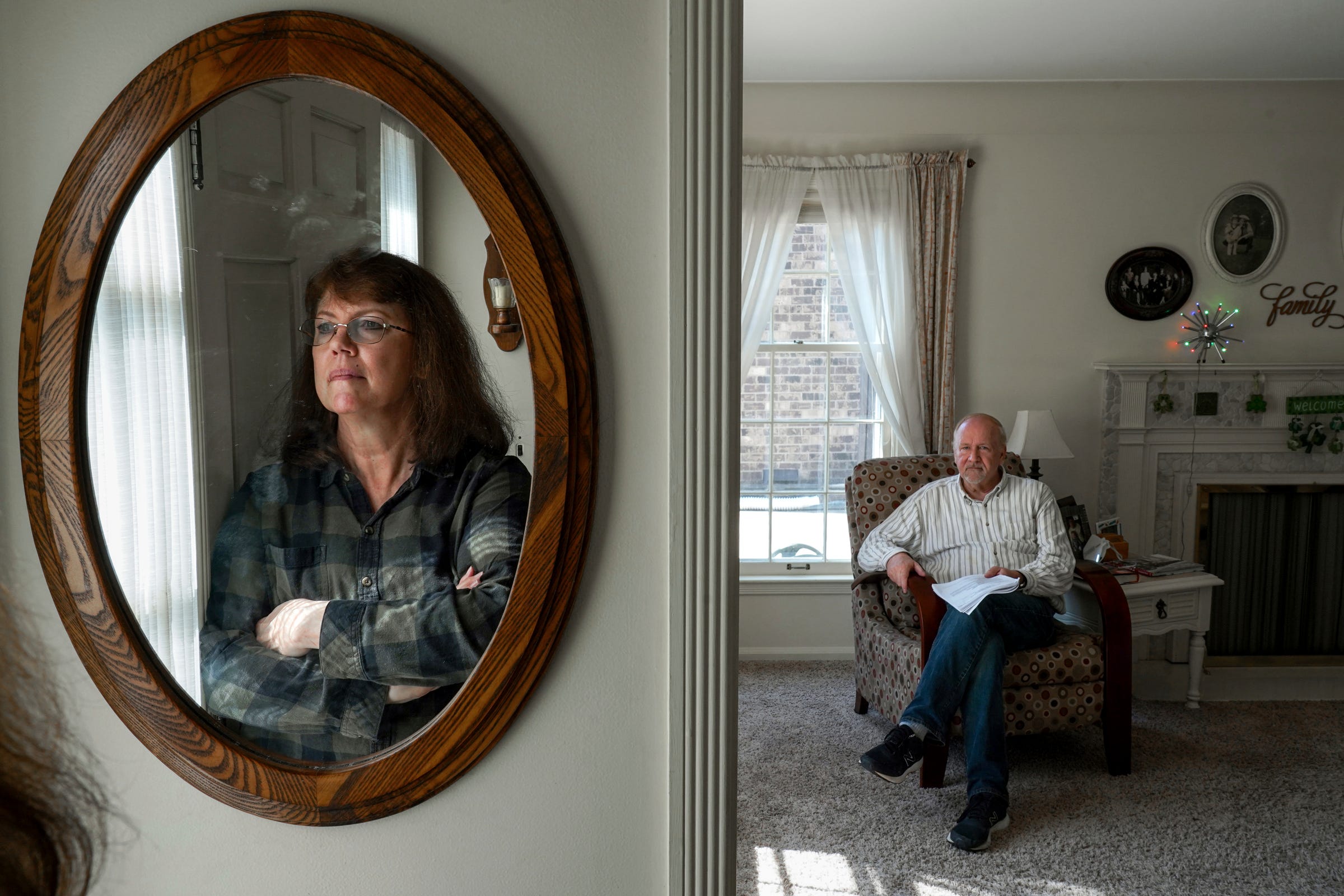 Cindy Berry, of Dearborn, stands before a mirror smudged with face prints from her autistic son as her husband, Doug Berry, sits in the living room of their home on Wednesday, March 16, 2022.