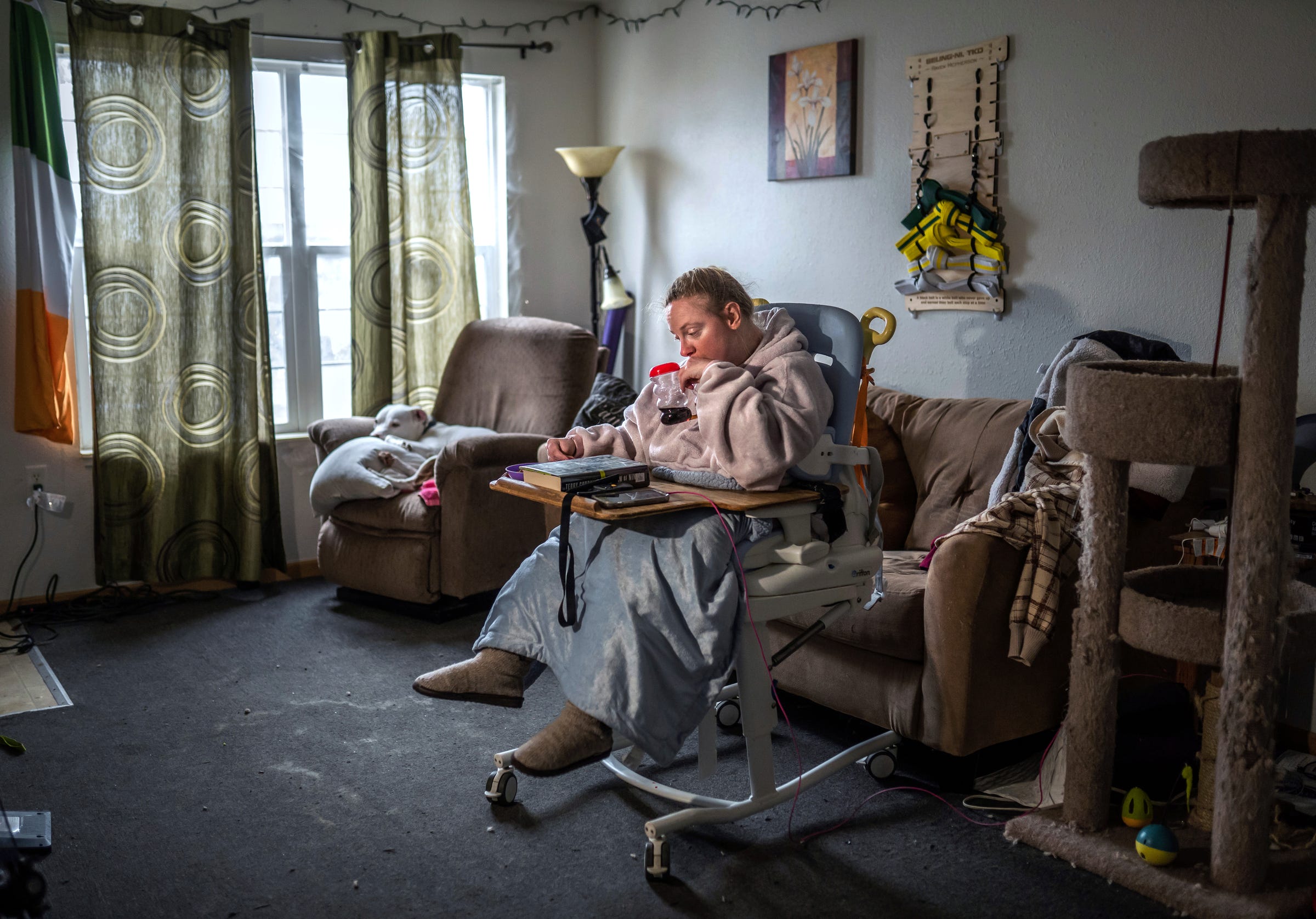 Cody Masson, 33, of Traverse City, sits on a commode seat in the living room of her apartment on Thursday, March 31, 2022, where she is left for hours in between shifts of caregivers.