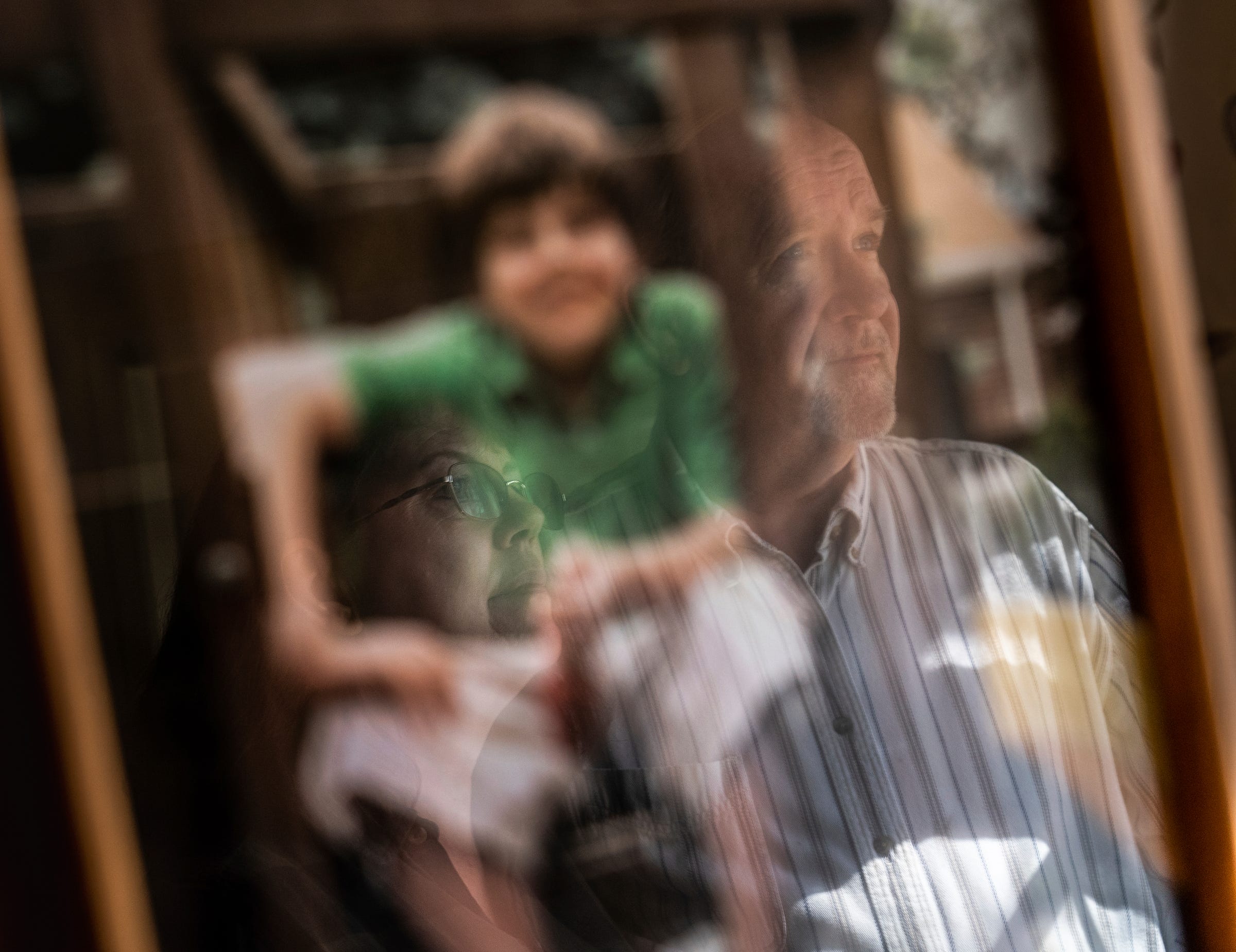 Cindy Berry and her husband, Doug, are seen reflected on an old photo of their son at their home on Wednesday, March 16, 2022. The Berrys say they don't understand why investigators in Wayne County failed to conclude that their son, who has autism, had been at grave risk in a vocational day program.