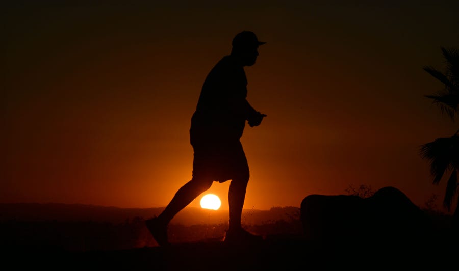 A hiker walks past the setting sun in Los Angeles, California on August 30, 2022. Forecasters said the mercury could reach as high as 112 Fahrenheit (44 Celsius) in the densely populated Los Angeles suburbs as a heat dome settles in over parts of California, Nevada and Arizona.