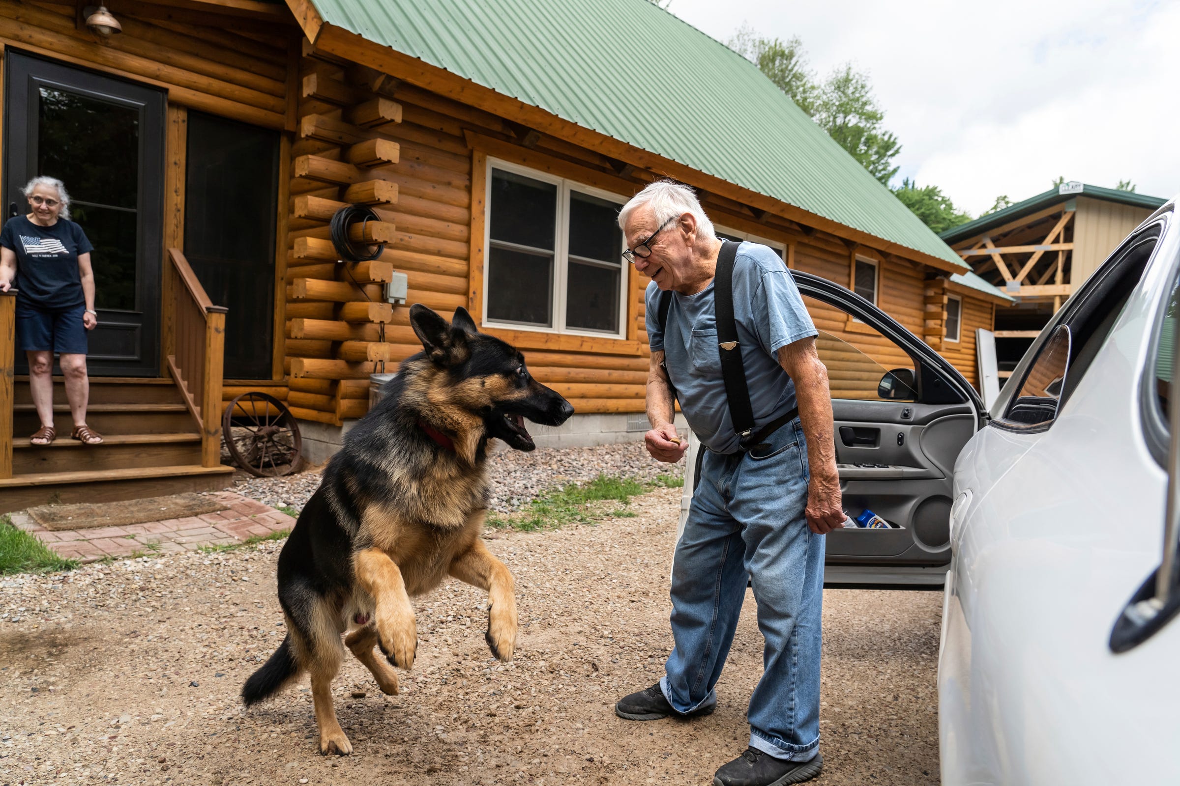 Mailman Ron Curtis, 86, holds a treat for an energetic German shepherd named Nuttah that he stops to visit along his postal route in Michigan's Upper Peninsula on Wednesday, July 27, 2022 as homeowner Leonor Hendrickson, 64, looks on.