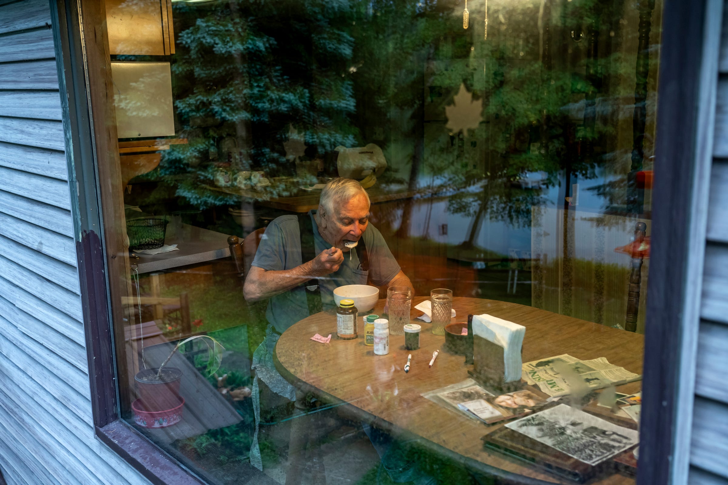 Ron Curtis, 86, of Wetmore starts his morning with a bowl of oatmeal while the view of Connor Lake, at the edge of his backyard, reflects off his dining room window on Wednesday, July 27, 2022. 