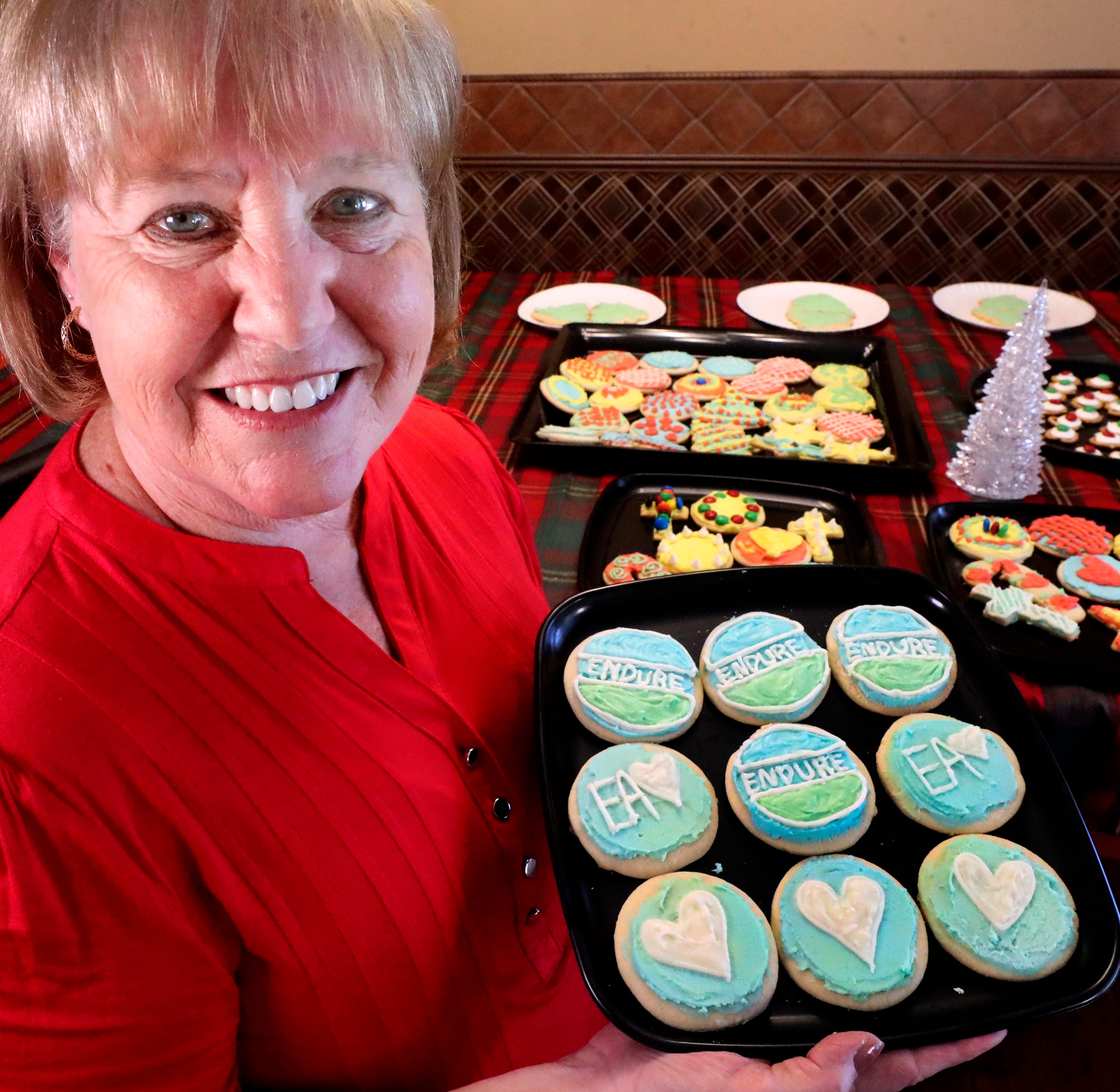 A woman holds a plate of decorated cookies.