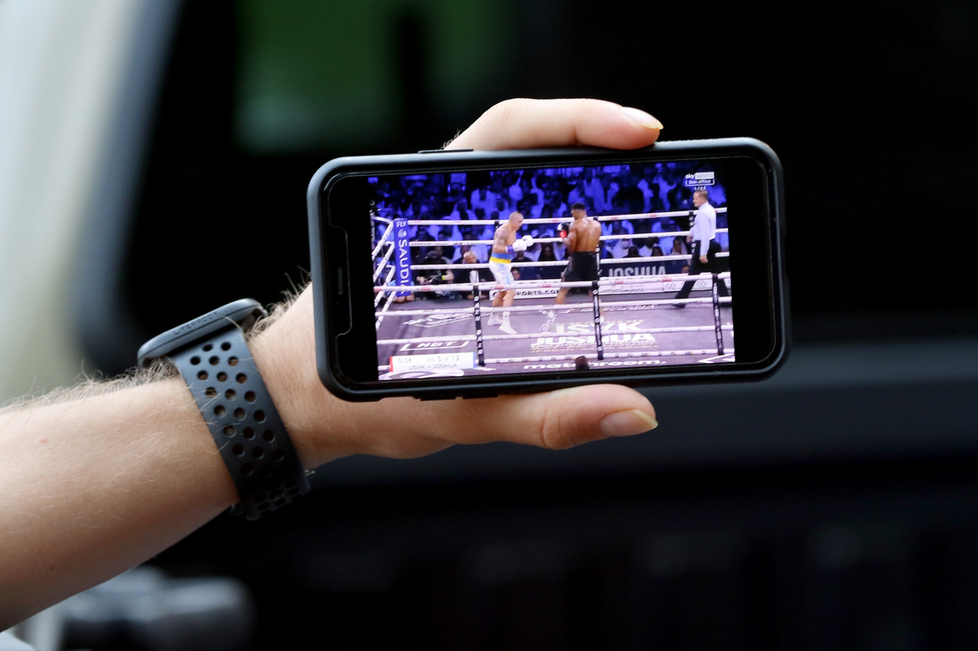 Ihor Sehinovych holds a smart phone for a group of people to watch Ukrainian boxer Oleksandr Usyk defend his boxing title on Saturday, Aug. 20, 2022.