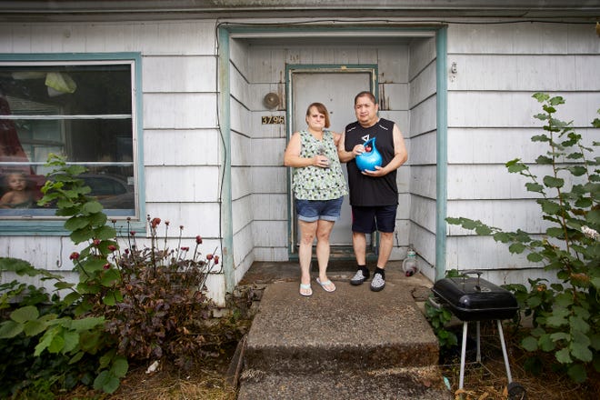 Misty Castillo, left, and her husband Arcadio stand in front of their home, holding the urn containing the ashes of their son Arcadio Castillo III, who was shot in 2021 by Salem police, as their granddaughter Nala, age 2, looks out the window in Salem on Aug. 18.