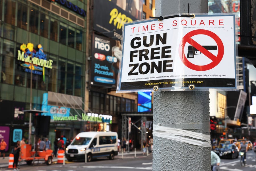 People walk past a "Gun Free Zone" sign posted on 40th Street and 7th Avenue on August 31, 2022 in New York City. Signs announcing a "gun-free zone" were posted at every entry and exit point of the Times Square area as a New York law limiting where firearms can be legally carried in public is set to go into effect on Thursday.