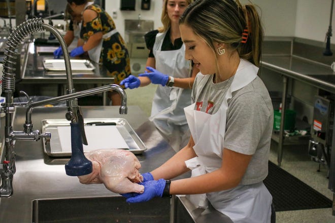 In this file photo, Micah Bixby, 17, takes a whole chicken out of its package as her lab partner Emma Holbert, 17 looks on in culinary arts class at Salina South High School.