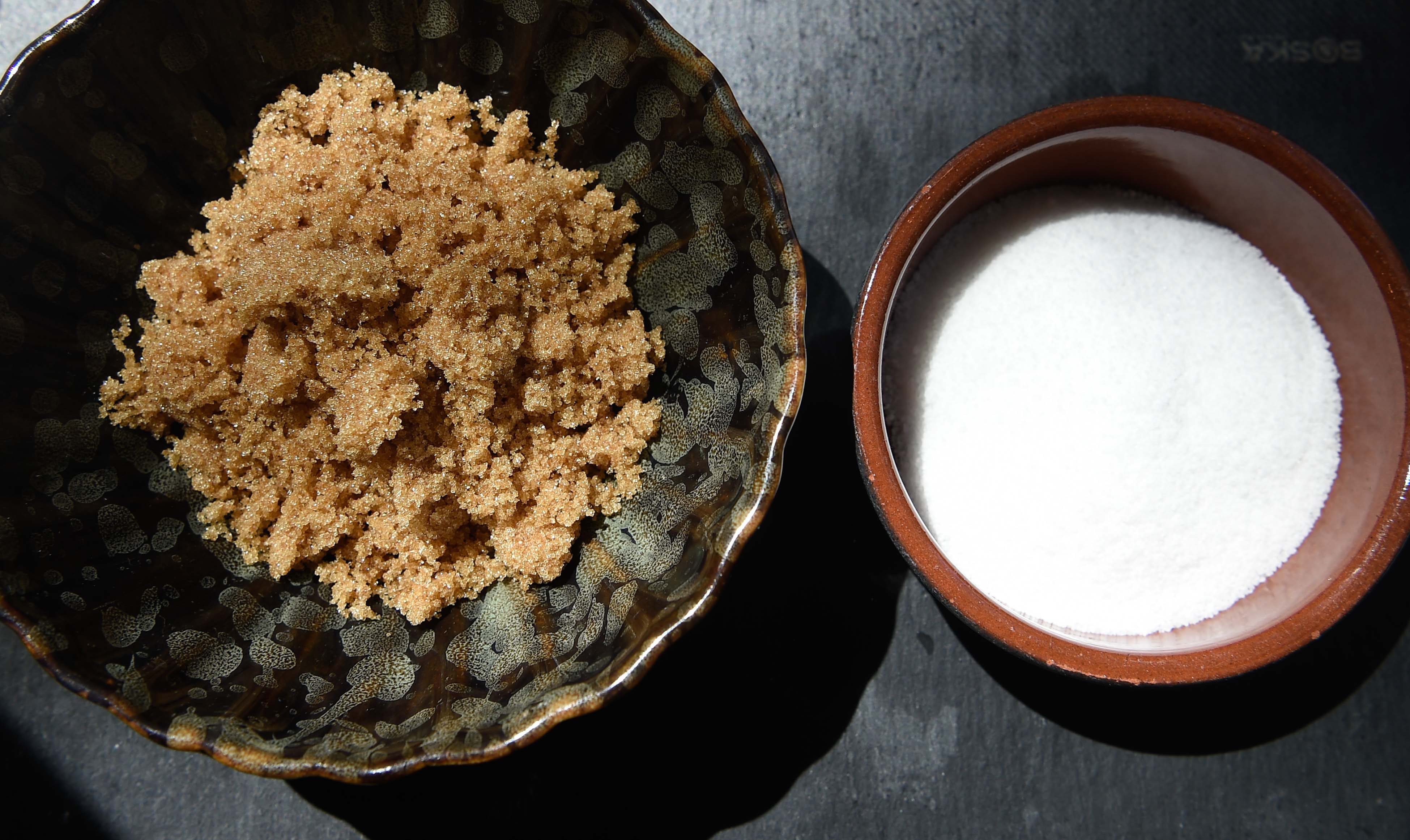 A bowl of brown sugar and a bowl of white sugar.