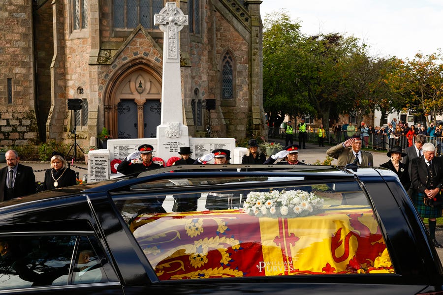 People salute as they stand in tribute as the cortege carrying the casket of the late Queen Elizabeth II passes by on September 11, 2022 in Ballater, United Kingdom.