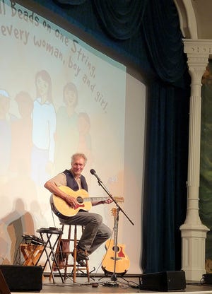 Musician and singer-storyteller Dennis Warner helps second graders sing the pages of his book, "Bead on One String" at the Goss on Tuesday.
