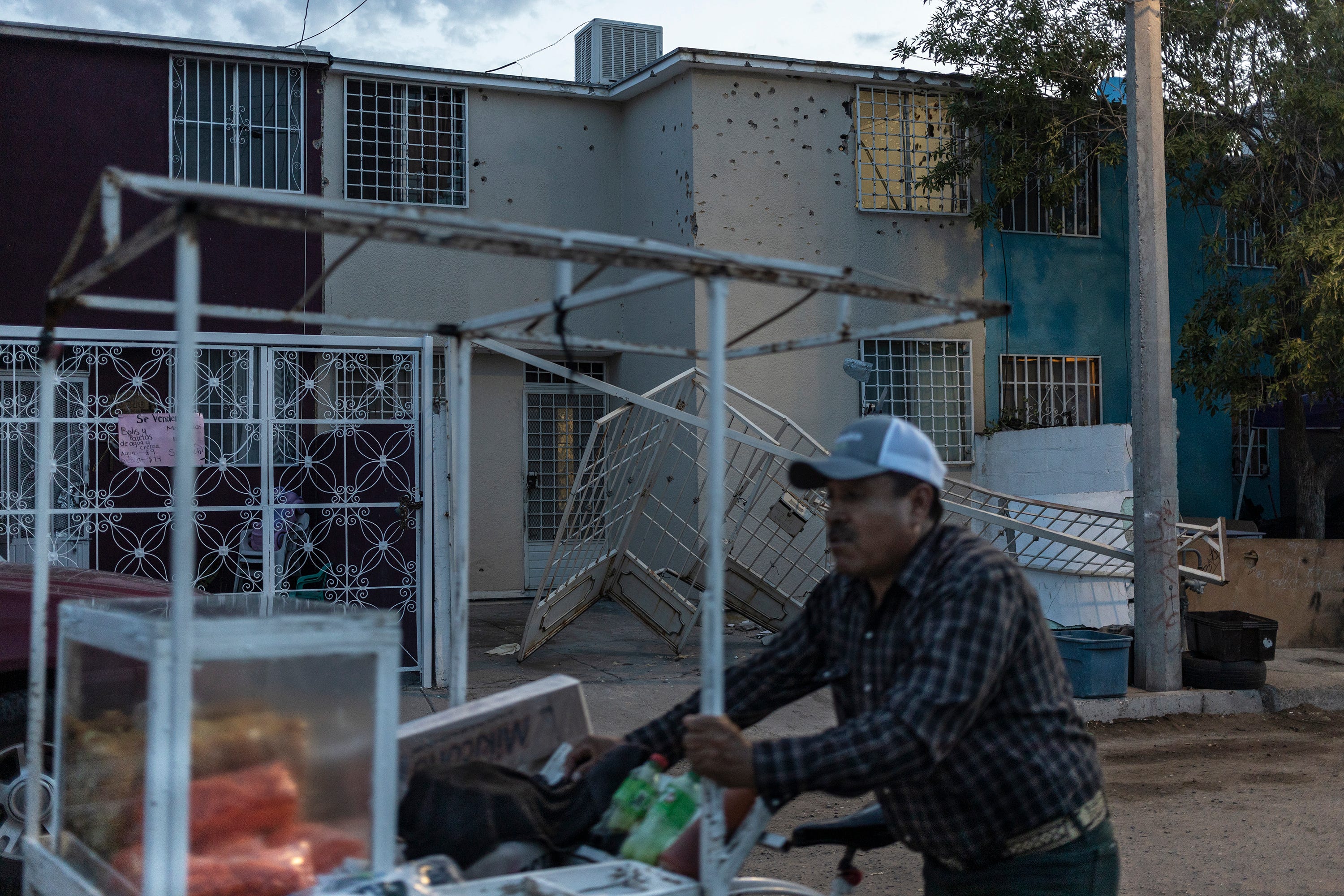 A snack vendor passes in front of the Ajenjo Street house, seen pockmarked by bullets, where police clashed with armed gang members and detained six after attacks on the people of Ciudad Juárez on Aug. 11, 2022.