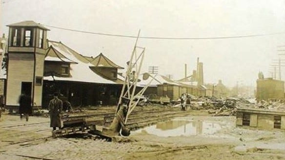The crossing tower was left standing, but the tracks are blocked and the gates have been damaged in this view north from State Street in the aftermath of the 1913 flood.  The distinctive depot occupied the northeast corner of State and Front streets during the first half of the 20th century.  The railroad crossing is still busy, but the site of the depot is now Tschumy Park.
