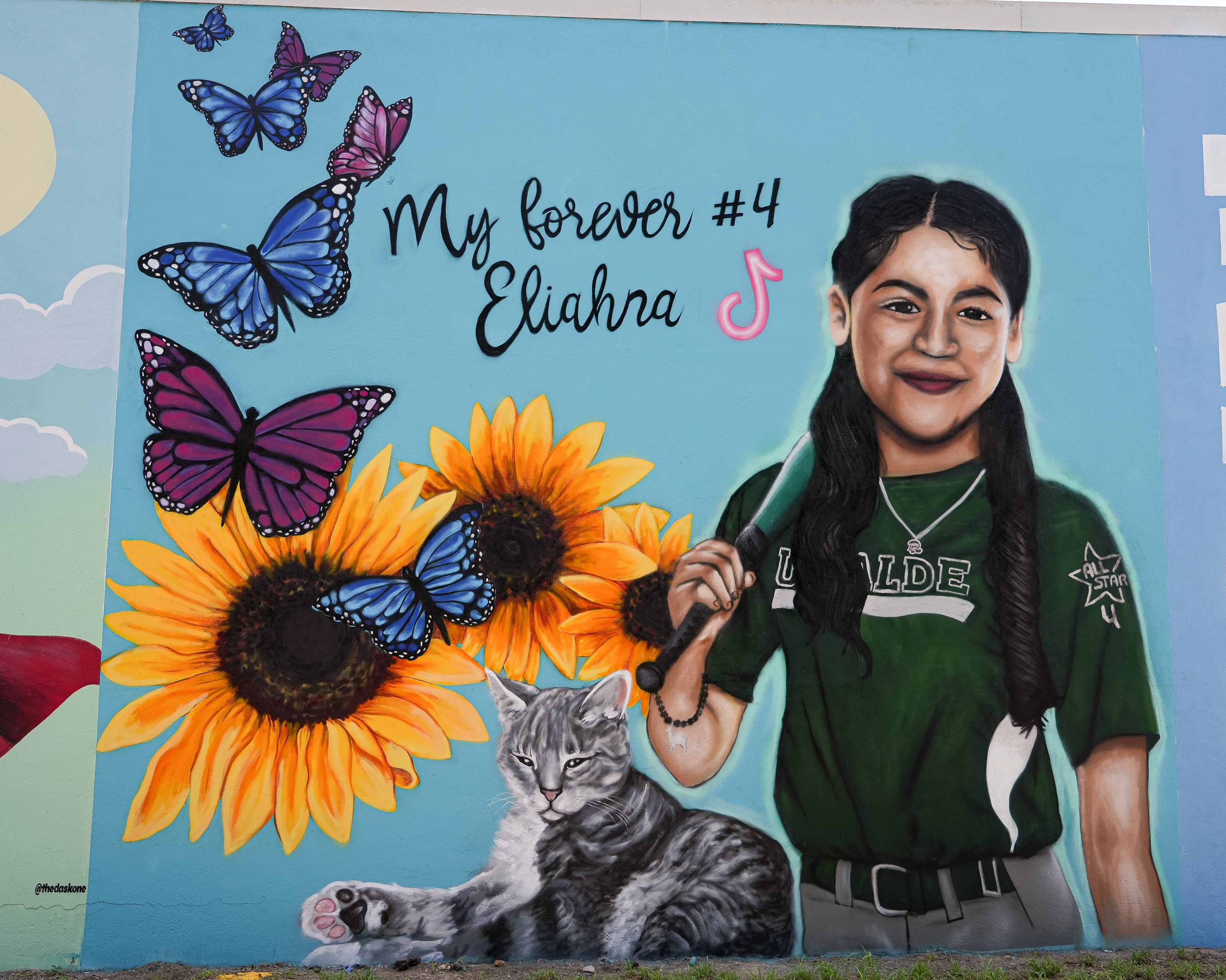 In her mural on the St. Henry de Osso building at 114 E. Nopal St., Eliahna Torres smiles proudly in her dark green Uvalde softball uniform with a bat slung over her shoulder.